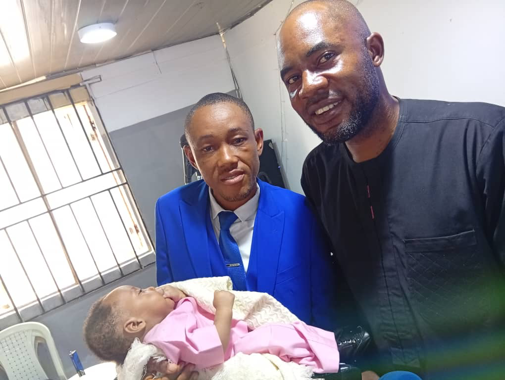 2 men standing carrying a baby